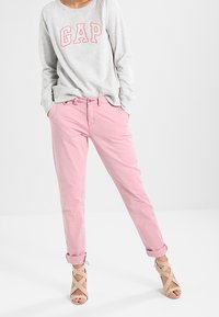 Maglietta grigia a maniche lunghe con logo "GAP", abbinata a pantaloni rosa arrotolati e sandali beige con cinturini. Outfit semplice e casual con texture morbide.