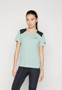 Lys mintgrønn atletisk t-skjorte med svarte skulderdetaljer, rosa piping, korte ermer og rund halslinning. Subtil logo på brystet.