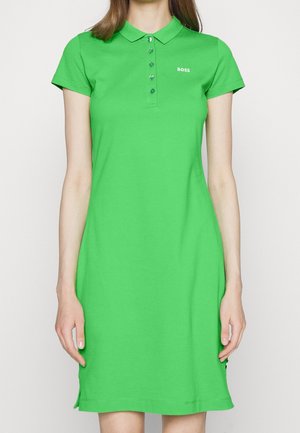 Mujer vistiendo un vestido tipo polo de manga corta color verde brillante con botones y el logo "BOSS" en el pecho, sobre un fondo liso.