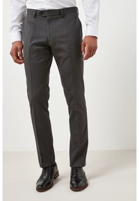Pantalones gris ajustados de corte entallado, con una textura suave, bolsillos frontales y una cinturilla. Llevados con zapatos de vestir negros.