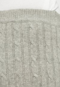 Tissu tricoté gris clair avec motif de torsades verticales et ceinture élastique côtelée, porté sur un haut blanc.