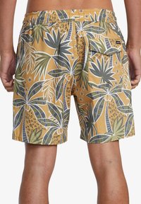 Costume da bagno da uomo in giallo senape con design di palme verdi e macchie di leopardato. Presenta una vita elasticizzata e una tasca posteriore.
