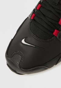 Svart joggesko med teksturert lærtå, mesh-overdel, røde lisser og en sydd hvit Nike-logo på siden.