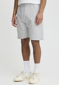 Shorts en coton gris avec une taille élastique et un cordon de serrage. Le mannequin porte des chaussettes blanches côtelées et des baskets blanches avec des accents crème.