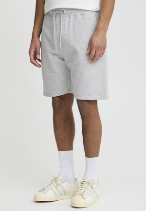 Grå bomullsshorts med elastisk midje og snor. Modellen har på seg hvite ribbestrikkede sokker og hvite joggesko med kremfargede detaljer.
