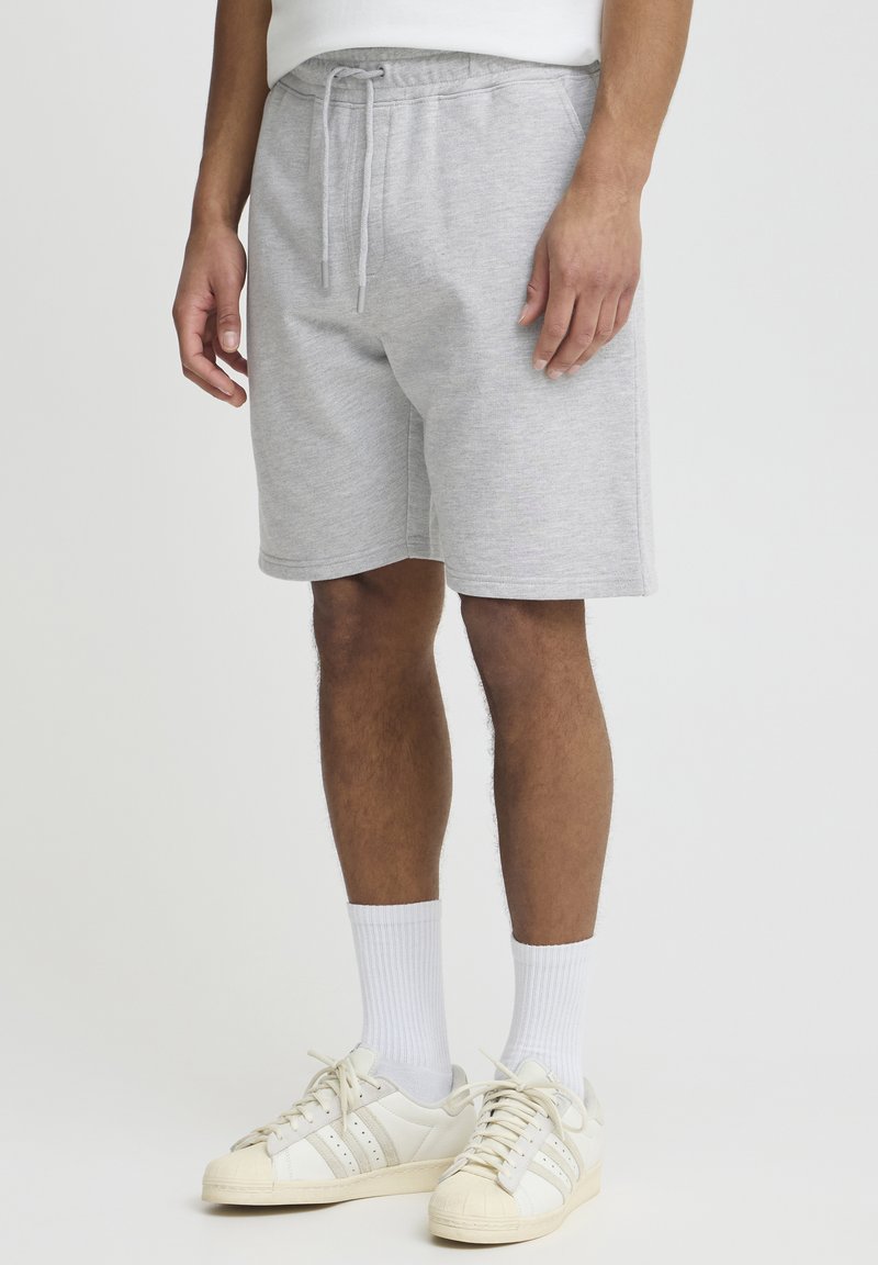 Shorts en coton gris avec une taille élastique et un cordon de serrage. Le mannequin porte des chaussettes blanches côtelées et des baskets blanches avec des accents crème.