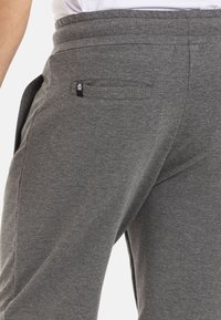 Graue Jersey-Stoff-Jogginghosen mit einem elastischen Bund, seitlichen Taschen und einem kleinen Logosticker auf der Gesäßtasche. Weiche und lockere Passform.