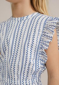 Rochie din țesătură albă cu buline albastre și modele de frunze, având mâneci volan și o talie elastică pentru un fit confortabil.