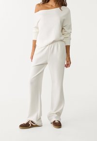 Sweatshirt blanc épaules dénudées à manches longues associé à un pantalon blanc ample et des baskets marron, en tissu léger texturé.