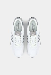 Pantofi sport albi cu accente gri, având trei dungi pe laterale, închidere cu șireturi și o textură de piele fină.