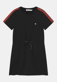 Černé bavlněné šaty s krátkým rukávem. Mají šňůrku v pase, ikonické logo na hrudi a červené značkové akcenty na rukávech.