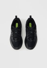 Μαύρα αθλητικά παπούτσια με επάνω μέρος από δίχτυ, υφασμάτινη λεπτομέρεια, στρογγυλεμένη μύτη και κορδόνια, με πράσινη εσωτερική σόλα που φέρει την ένδειξη "TRAIL".