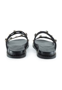 Schwarze Leder-Sandalen mit zwei breiten Riemen, verziert mit runden goldenen Akzenten. Flache Sohle mit strukturiertem Fußbett und kontrastierenden Nähten.