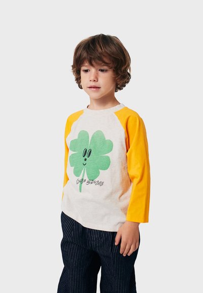 Long-sleeve T-shirt featuring a green clover graphic on beige fabric with yellow sleeves. Text below clover reads "Bobo Choses."