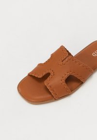 Brune lærersandaler med udskæringsdesign og dekorativ syning. Flad sål, firkantet tåform og glat tekstur.