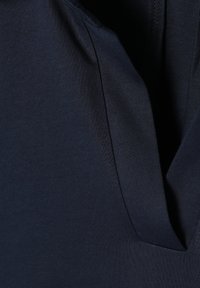 Marineblauwe stof met een gladde textuur, voorzien van een rechte halslijn en een zijnaaddetail, wat wijst op een eenvoudig, minimalistisch ontwerp.