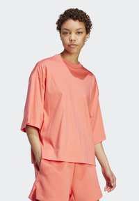 Korálová oversized tričko vyrobené z bavlny, s krátkymi širokými rukávmi a zaobleným výstrihom. V kombinácii s ladiacimi šortkami.