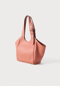 Nježna ružičasta kožna torba s podesivim dvostrukim remenom i suptilno urezanim logotipom sprijeda, fotografirana na jednostavnoj bijeloj pozadini.