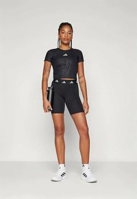 Μαύρο αθλητικό κοντό τοπ με υφή, συνδυασμένο με μαύρες σορτς και λευκά αθλητικά παπούτσια, φέροντας λογότυπα της μάρκας σε λευκό χρώμα.