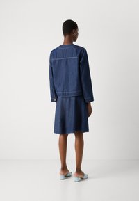 Denimkjole med lange ermer, innsnevret midje og utsvingt skjørt. Mørkeblå farge med synlig søm. Blå åpen helsestøvler med hæl.