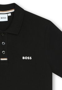Polo noir en tissu texturé, avec un col classique, une patte de boutonnage à trois boutons et un logo "BOSS" blanc sur la poitrine.