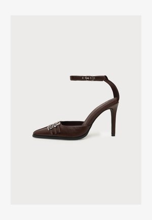 Chaussure à talon haut en cuir marron avec bout pointu, trois boucles décoratives argentées à l'avant et bride à la cheville avec boucle argentée.