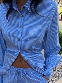 Camisa azul riscada com pequenos adornos prateados, combinada com calças correspondentes, apresentando um cós elástico e cordão.