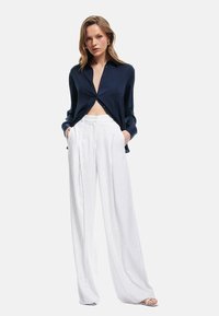 Navy button-down shirt with a cropped cut, paired with white vertical-striped wide-leg pants. Smooth fabric with a tailored fit.