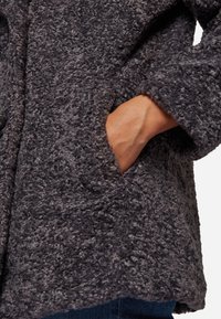 Gray fluffy coat with textured fabric, featuring a relaxed fit, wide sleeves, and hidden side pockets. Detailed stitching along the edges.