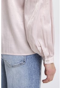 Light pink blouse made of satin, featuring puffed sleeves and scattered rhinestones. Button detail on the cuff and a relaxed fit.