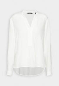 Blouse blanche à manches longues avec col en V, sans col et ourlet légèrement arrondi, présentée sur un fond uni.