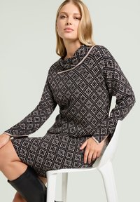 Zwart crèmekleurige jurk met een patroon, een col hals, lange mouwen en een nauwsluitend ontwerp. Gemaakt van textuurstof met een geometrisch diamantpatroon.