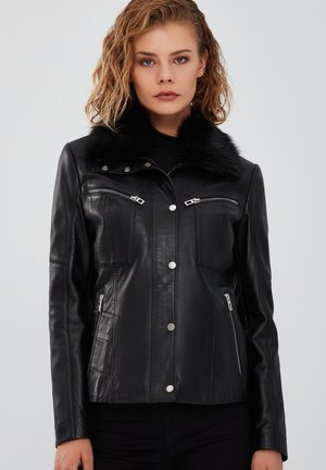 Giubbotto di pelle nera con collare in pelliccia sintetica, hardware argentato, tasche con zip e vestibilità su misura. Texture liscia con dettagli cuciti.
