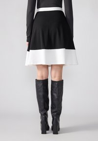 Jupe évasée noire avec un ourlet blanc, fabriquée en tissu lisse. Dispose d'une taille ajustée et d'un design superposé. Associée à des bottes noires à hauteur de genou.