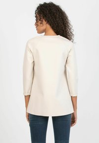 Beige synthetic three-quarter sleeve top with a curved hem and rolled cuffs, featuring a rounded neckline and smooth texture.