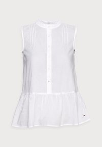 Chemise sans manches blanche avec un col haut, devant boutonné et plis. Présente un ourlet évasé et des logos subtils; fabriquée en tissu léger.