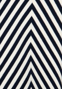 Pletená látka s vzorem do V, se střídajícími námořnickými modrými a krémovými pruhy. Textura je měkká a hladká, s jasně vymezenými okraji.