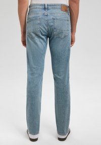 Vaqueros de mezclilla azul claro con corte recto, cinco bolsillos y una parche de cuero marrón en la cintura trasera. Textura suave y ligero desgaste.