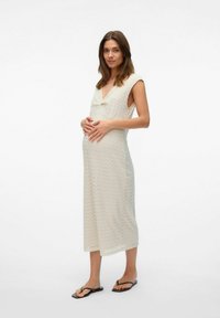 Robe tricotée légère de couleur crème avec un décolleté en V, des manches courtes et un motif en zigzag ; portée par un modèle enceinte avec des sandales plates.