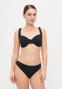 Juodas bikini rinkinys, turintis struktūrizuotą liemenėlę su plačiomis juostelėmis ir be siūlių aukštų liemenių kelnaitėmis, pagamintas iš lygaus, elastingo medžiagos.