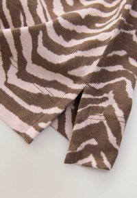 Prim-plan al unui material cu imprimeu de zebra în nuanțe de maro și bej, cu margini cusute și un detaliu mic de tăietură.