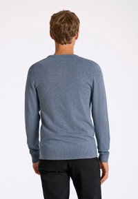 Maglione blu lavorato a maglia con scollo rotondo, maniche lunghe e polsini a coste. Presenta una texture sottile. Indossato con pantaloni neri.