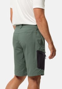 Pantaloni corti verdi da uomo, realizzati in tessuto leggero, con una tasca laterale con zip nera e una texture liscia. Lunghezza corta con una vestibilità su misura.