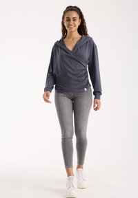 Donkergrijze hoody wraptop met lange mouwen, gecombineerd met grijze skinny jeans en witte sneakers. Glad textuur met gedrapeerd materiaal.