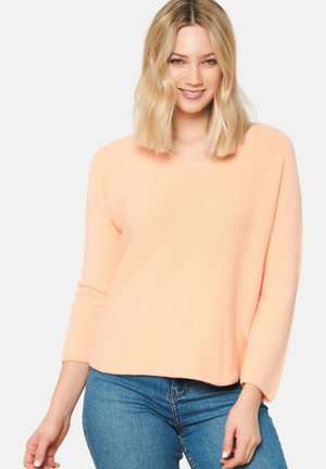 Peach-colored, soft sweater with a V-neck and long sleeves, crafted from a textured knit fabric. Paired with denim jeans.
