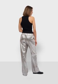Metalen zilveren broek met een relaxte pasvorm, elastische tailleband en een soepele textuur, gecombineerd met een zwart mouwloos topje.