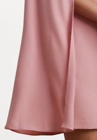Vestido rosa claro hecho de una tela suave, con un diseño fluido y un dobladillo ligeramente acampanado. Líneas simples y limpias sin adornos.