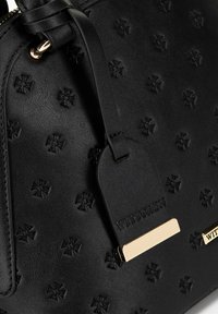 Zwarte handtas van gestructureerd leer, met geperste bloemenpatronen, goudkleurige hardware en een hangende merketiket.