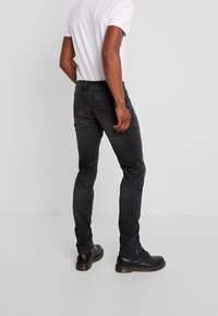 Svarta denimjeans med slim fit, med en medelhög midja, subtila blekningar och förstärkt sömnad, tillsammans med svarta stövlar.