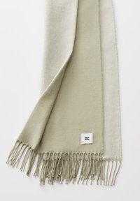 Lichtbeige zachte sjaal met gedraaide franjes en een klein wit label met een zwart abstract logo op een witte achtergrond.